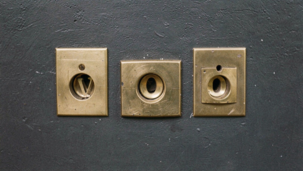 Three brass letter slots of different sizes set into a dark painted wall, photographed straight on.